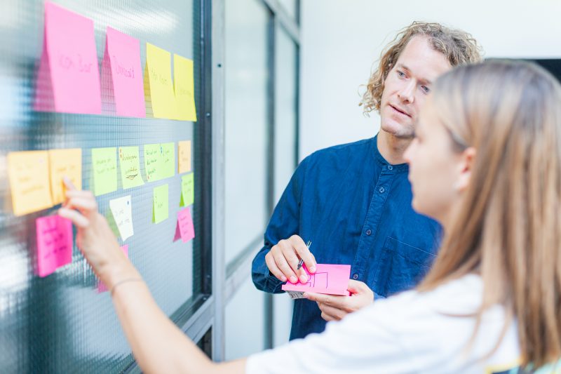 Two UX Designers organizing post-it ideas on a wall during a design workshop.