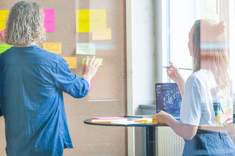 Designer ordnen Post-it-Ideen an einer Wand während eines Workshops.